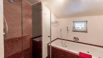 Ein Badezimmer mit Duschkabine aus Glas, einer Badewanne und einem roten Handtuch sowie einem Fenster über der Wanne.