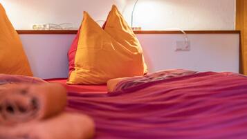 A bed with orange and red pillows, a wooden headboard, and a wall socket.