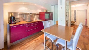 Een moderne keuken met een houten tafel en witte stoelen, een rode kast en roestvrijstalen apparatuur.