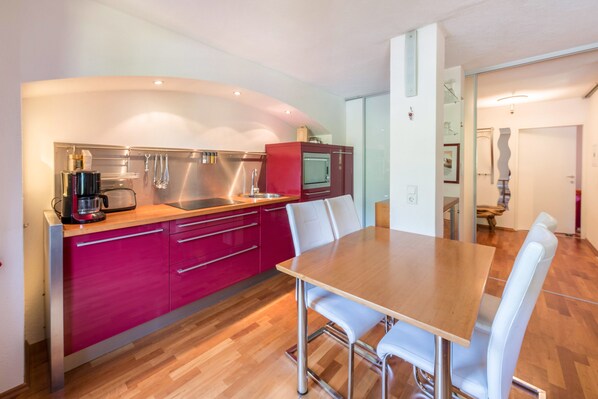 A modern kitchen with a wooden table and white chairs, a red cabinet, and stainless steel appliances.