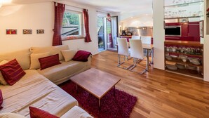 Een moderne woonkamer met een bank, salontafel en een keukenhoek met glazen schappen.