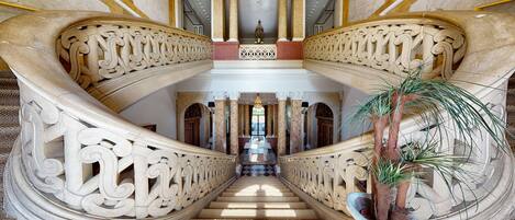 A grand staircase with ornate balustrades and a central column, leading to a landing with a chandelier.