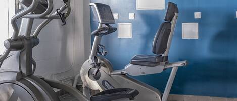 Ein Fitnessraum mit Ergometer und Laufband, eine blaue Wand mit einer Union-Jack-Flagge und ein Fenster mit Jalousien.