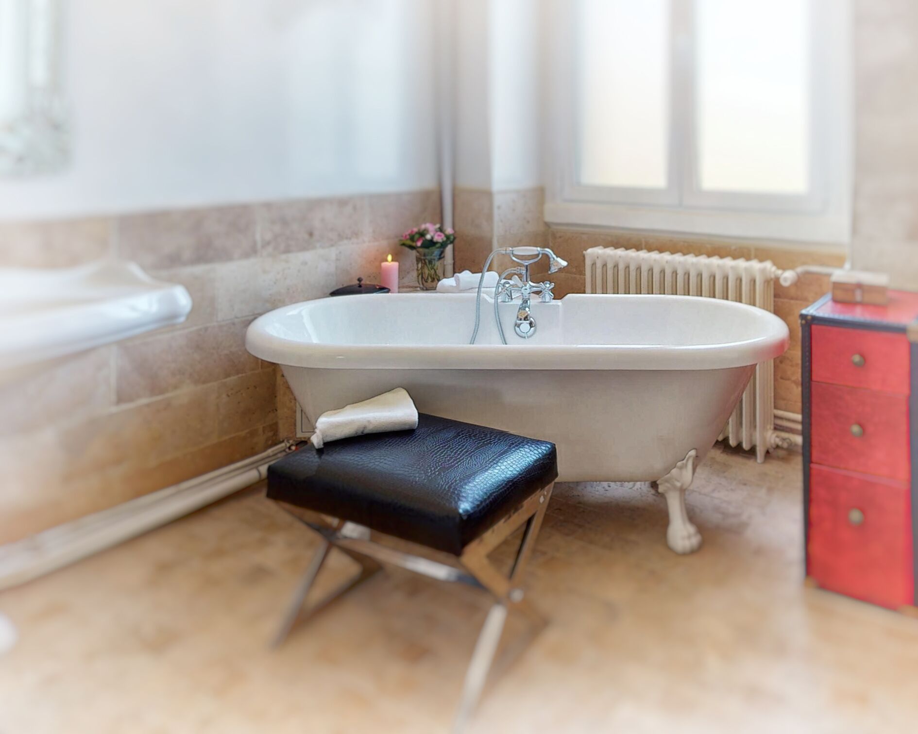 A bathroom with a freestanding bathtub, a red dresser, and a window providing natural light.