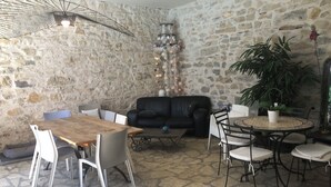 A cozy interior with a stone wall, a black leather sofa, a wooden dining table, and a round table with chairs. - Chambre d'hôtes Bleus Matines (Caveirac)