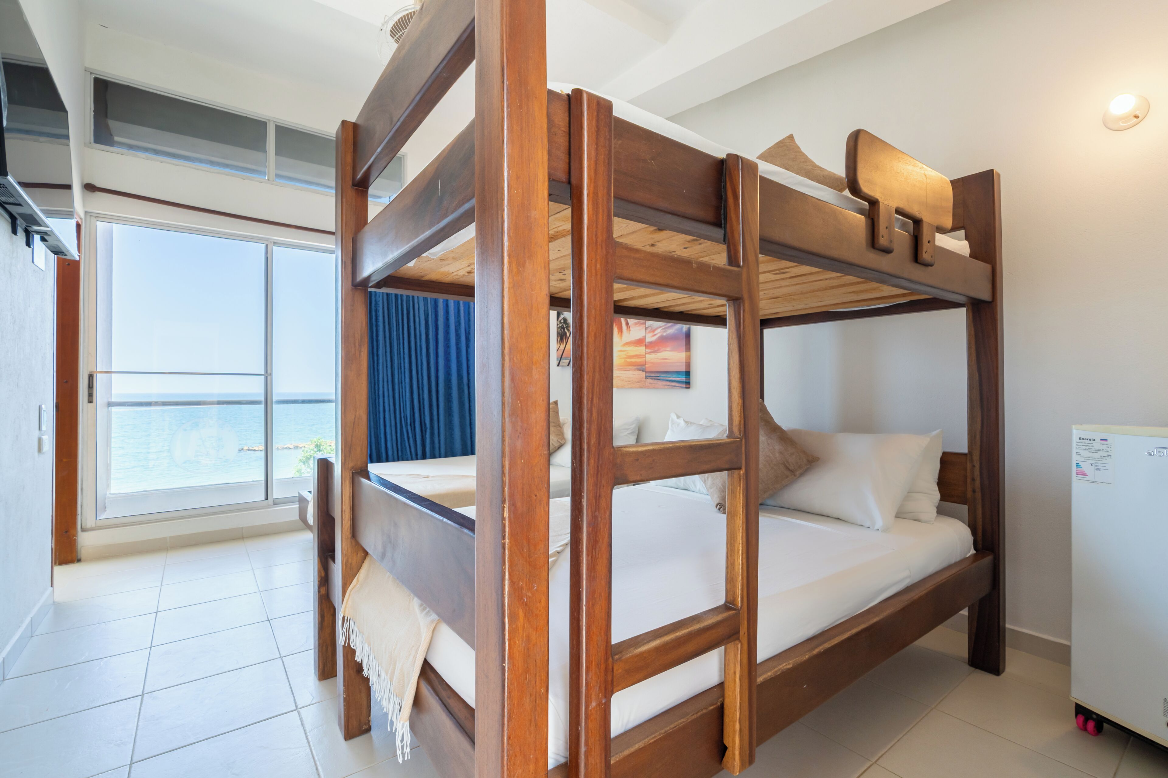 A bunk bed room with a view of the sea, a window, and a refrigerator.