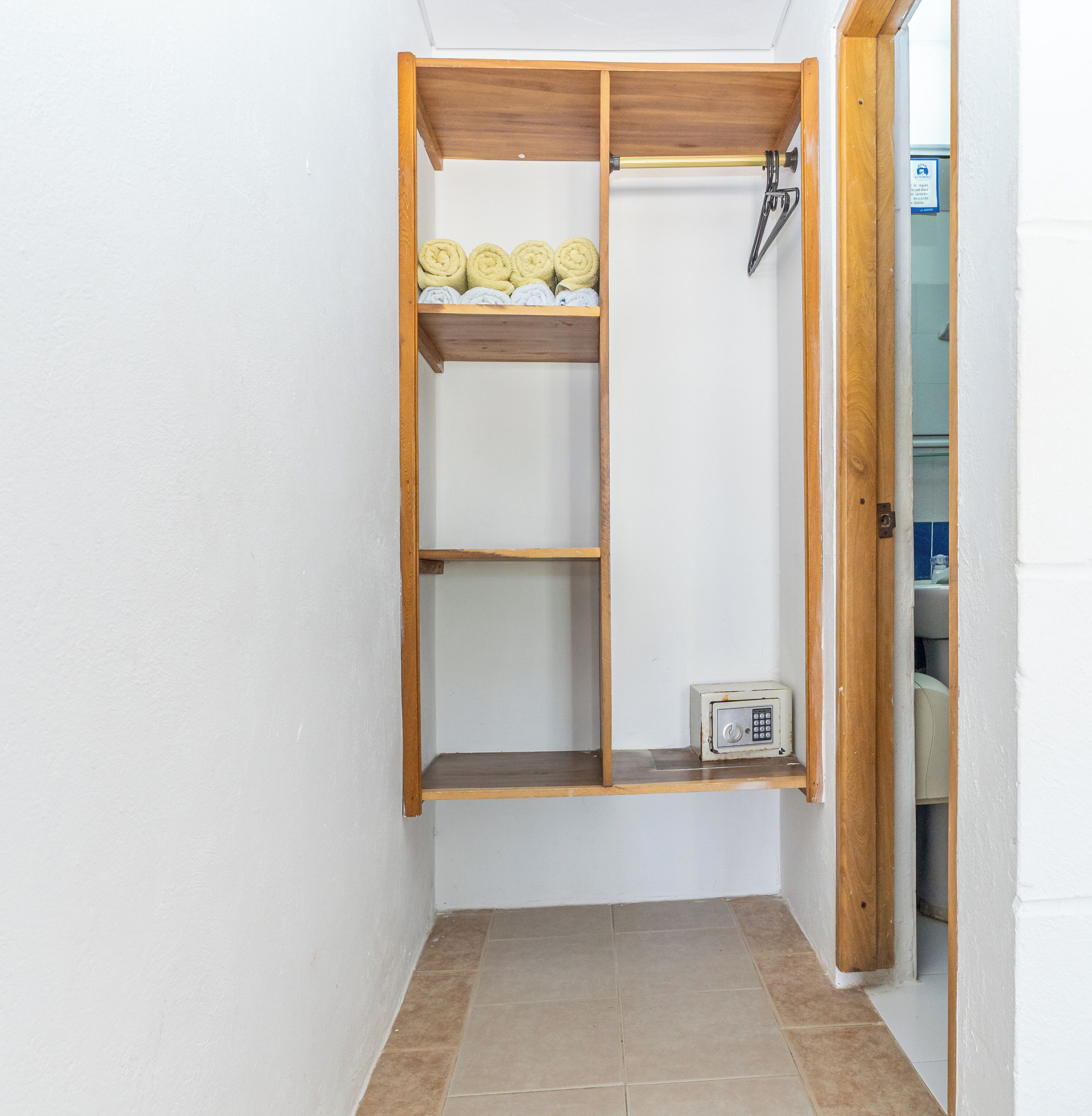 A wooden wardrobe with shelves and a hanging rod, a small safe, and a metal hook.