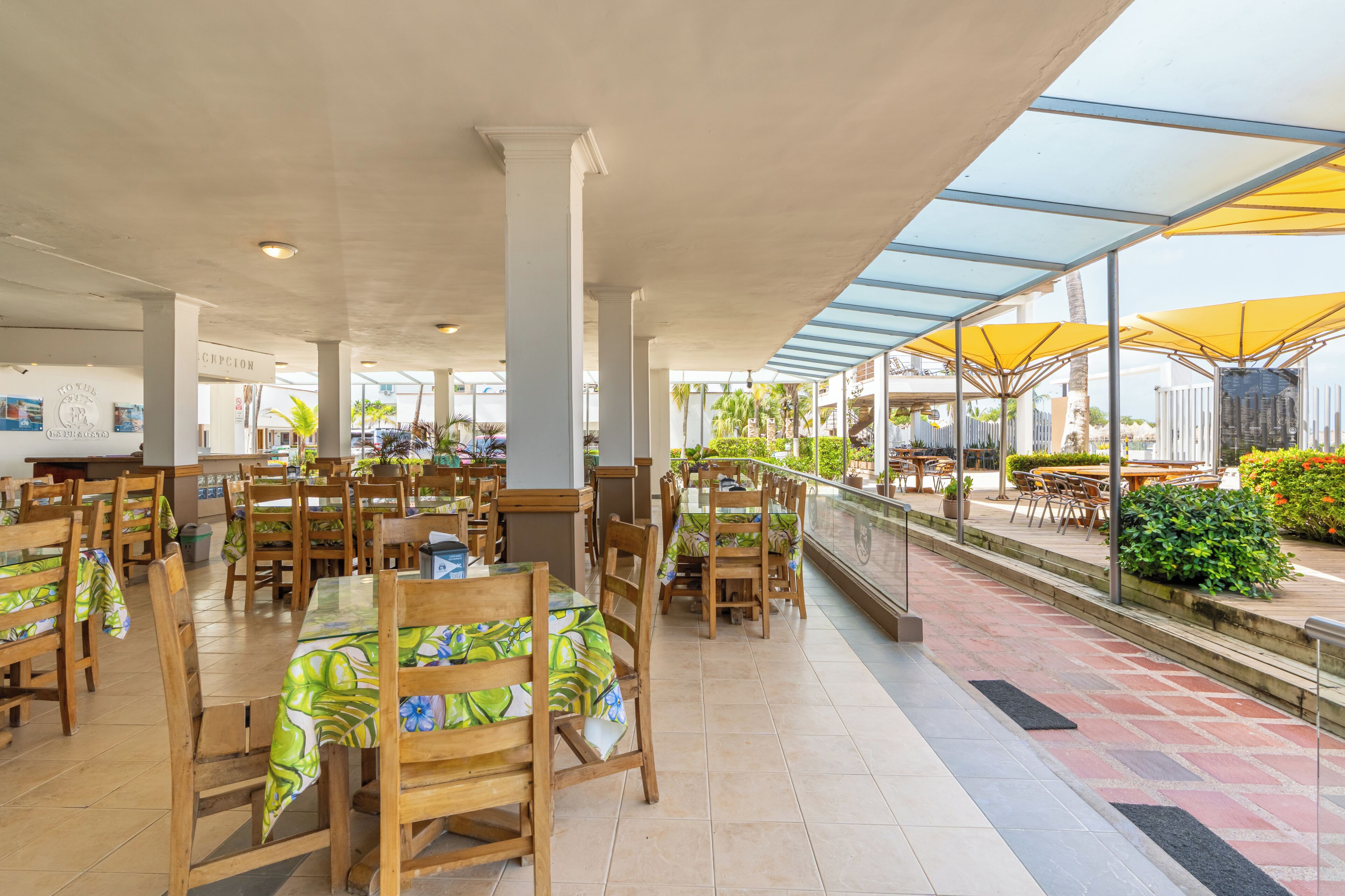Ein Essbereich mit Holztischen und -stühlen, eine Rezeption und Blick auf die Außenpatiofläche.