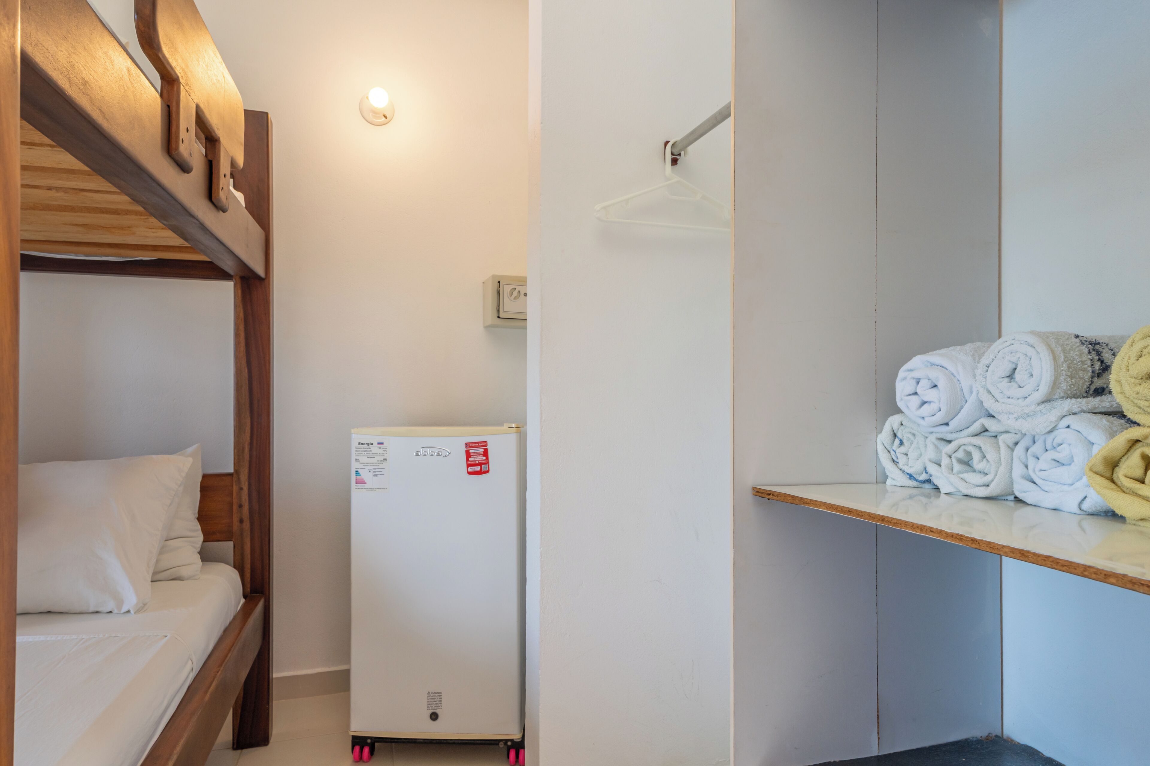 Un dormitorio con una cama litera, un refrigerador blanco y un estante con toallas dobladas.