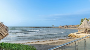 A beach view with thatched-roof huts, a sandy beach, and a rocky shoreline. - Hotel La Fragata Coveñas (Coveñas)