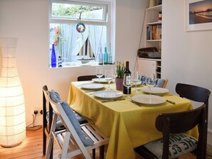 Un comedor con una mesa lista para cuatro personas, una planta en maceta y una botella de vino.