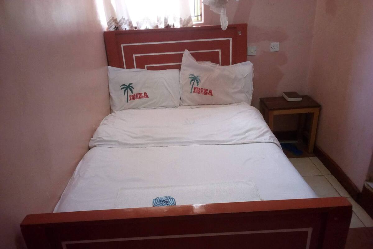 En säng med vita sängkläder och två kuddar med texten ”IBIZA” och palmmotiv.