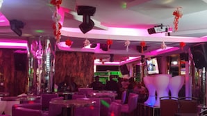 Un bar con tavoli e sedie rotonde, illuminazione rosa ed elementi decorativi come fiori e luci a soffitto.