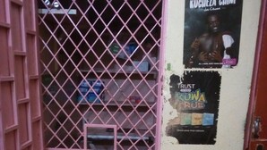 Una porta rosa con una griglia metallica, un manifesto appeso al muro e un piccolo ripiano con oggetti dietro la griglia.