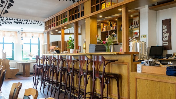 A restaurant interior with wooden bar stools, a counter with bottles, and a computer on the counter. - Nordstern Restaurant & Pension (Gingst)