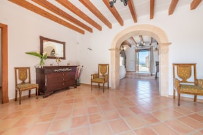 A spacious room with a tiled floor, wooden furniture, and an arched doorway leading to another area.