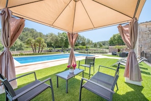 A poolside area with a covered seating area, a pool, and a well-maintained lawn.