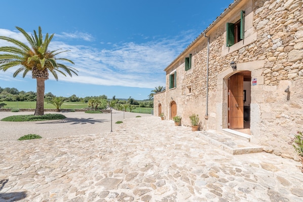 A stone building with a wooden door, a palm tree, and a clear sky.