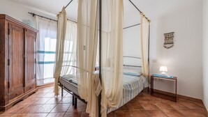 Un dormitorio con cama con dosel, un armario de madera, una mesita de noche con lámpara y un adorno de macramé en la pared.