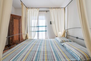 Ein Schlafzimmer mit Bett, Vorhängen, einem Holzschrank und einem Fenster.