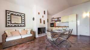 Una sala de estar con sofá, mesa de comedor, sillas, chimenea, zona de cocina y decoración en las paredes.