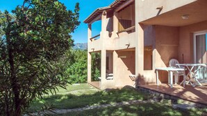 Un edificio de dos pisos con un patio, mobiliario exterior y vistas a la vegetación y montañas circundantes.