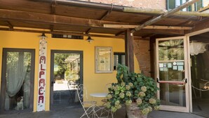 Un bâtiment jaune avec une pergola en bois, une porte en verre et une enseigne dont le texte est partiellement visible.