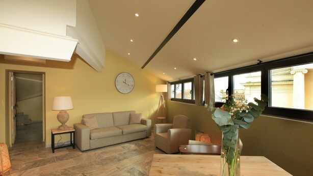 A spacious living room with a sofa, armchair, and a wooden coffee table. A clock is mounted on the wall, and a vase with flowers is on the table. - New in 2020, 5 guest rooms, tastefully decorated, ideal location! (saint remy de provence)