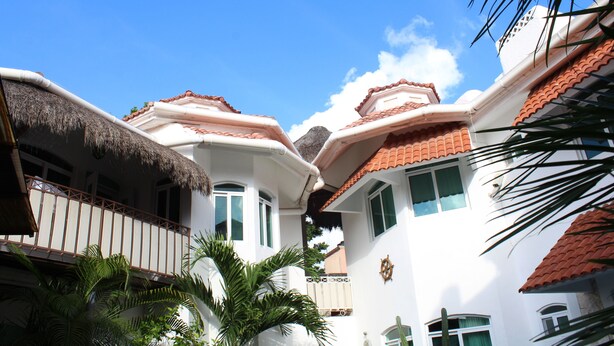A white building with red-tiled roofs and a thatched roof balcony. - Casa Mandarina Cozumel (Cozumel)