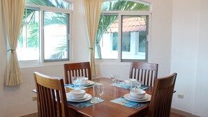 A dining table set for four with chairs, positioned near windows with curtains. - Casa Mandarina Cozumel (Cozumel)