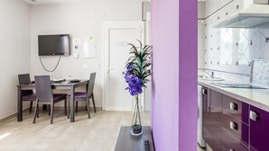A modern room with a dining area, a TV mounted on the wall, a vase with flowers, and a kitchen with a purple accent wall. - Modern, with roof terrace and very close to the beach - Apartamento Caviar (Conil de la Frontera)
