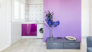 A modern kitchen with a washing machine, a purple wall, and a vase with flowers. - Modern, with roof terrace and very close to the beach - Apartamento Caviar (Conil de la Frontera)