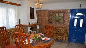 Un coin repas avec une table ronde en bois, dressée pour quatre personnes, entourée de chaises en bois. On aperçoit une porte bleue et un mur à motifs à l’arrière-plan.