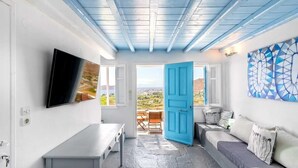 Une pièce avec un plafond bleu, un téléviseur fixé au mur, une porte bleue, un canapé et une vue sur le paysage par la porte.