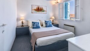 Une chambre à coucher avec un lit, des lampes de chevet, un tableau, une fenêtre avec des volets bleus et une vue sur le paysage.