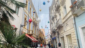 Una calle estrecha bordeada de cafés y tiendas, con mesas al aire libre y coloridas decoraciones colgantes.