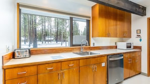 Une cuisine moderne avec des meubles en bois, un lave-vaisselle en acier inoxydable, un four à micro-ondes et une grande fenêtre donnant sur une forêt enneigée.