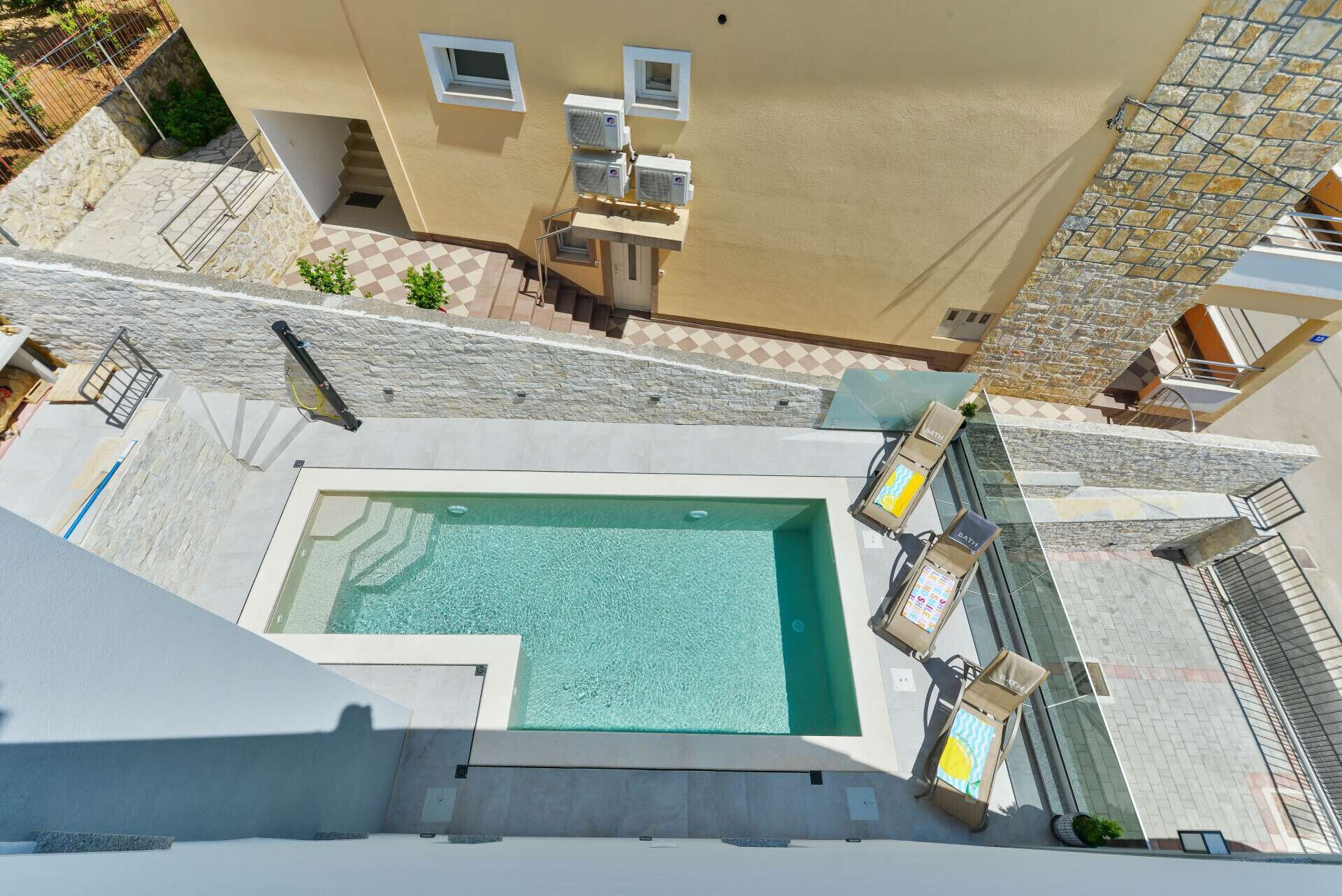 An aerial view of a hotel with a swimming pool, outdoor seating, and a stone wall.