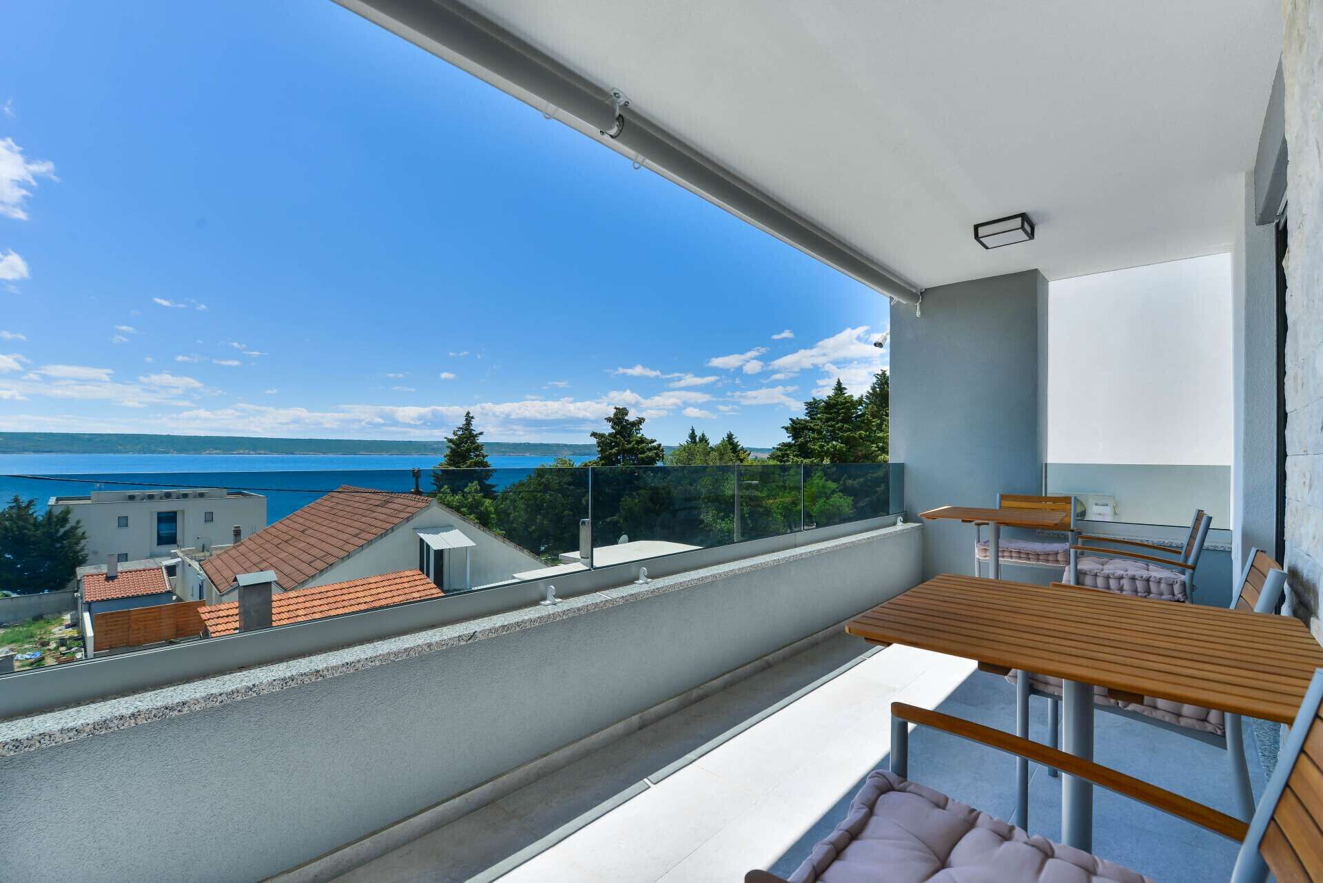 A balcony with a view of the sea, a table, and a chair.