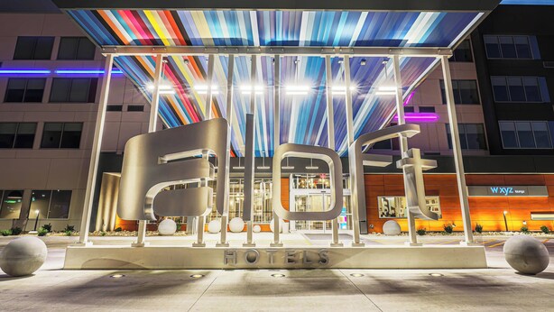Une entrée d’hôtel moderne, avec un toit rayé aux couleurs vives, une enseigne lumineuse et un grand panneau indiquant « HÔTELS ».