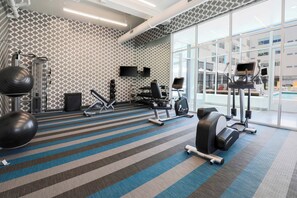 Een fitnessruimte met diverse trainingsapparaten, een behangwand en grote ramen.