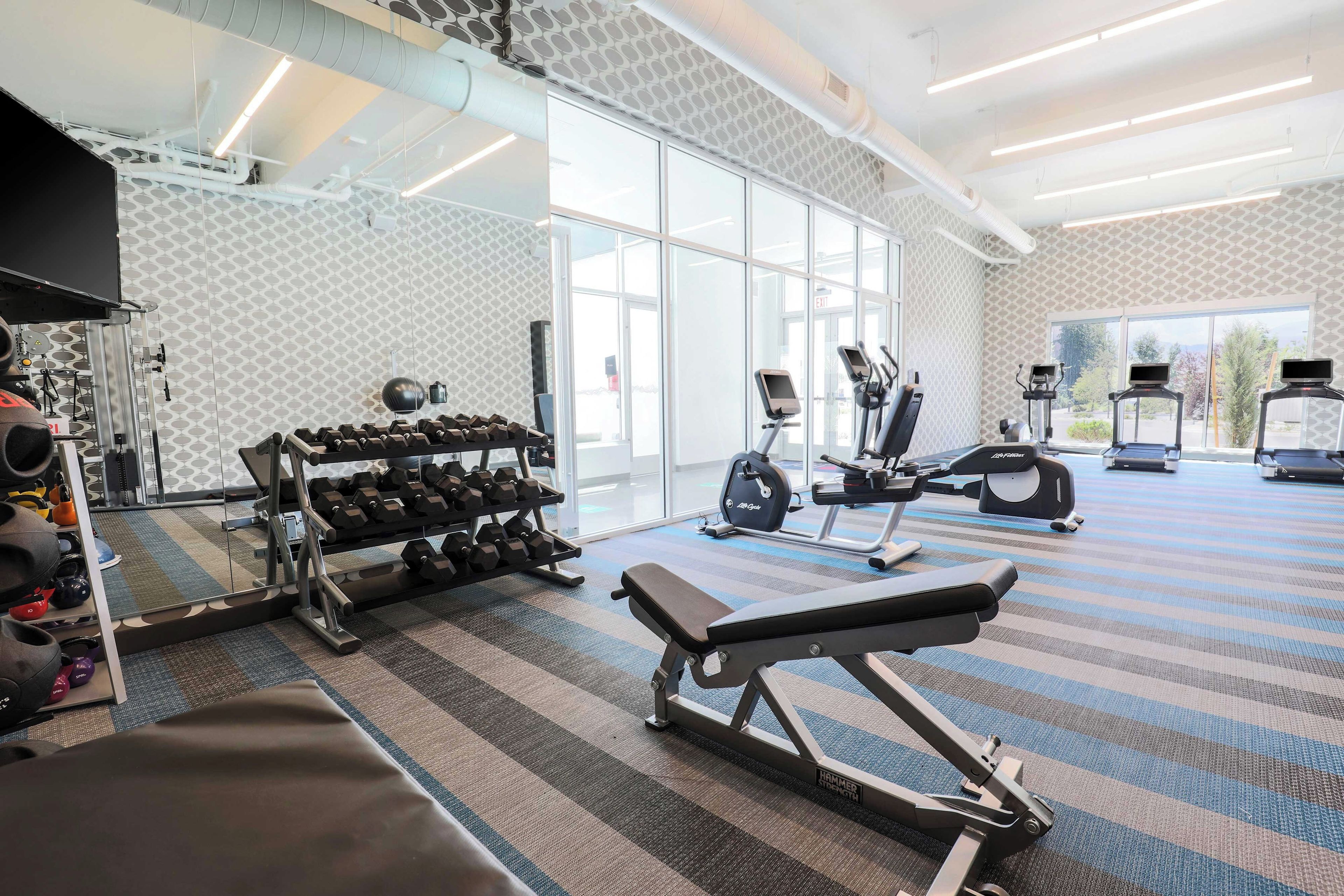 A gym with exercise equipment, a bench, and a mirrored wall.