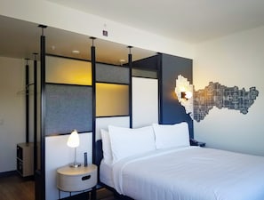 Una camera d'albergo moderna con un letto, un comodino con una lampada, un punto luce a parete e un lampadario.