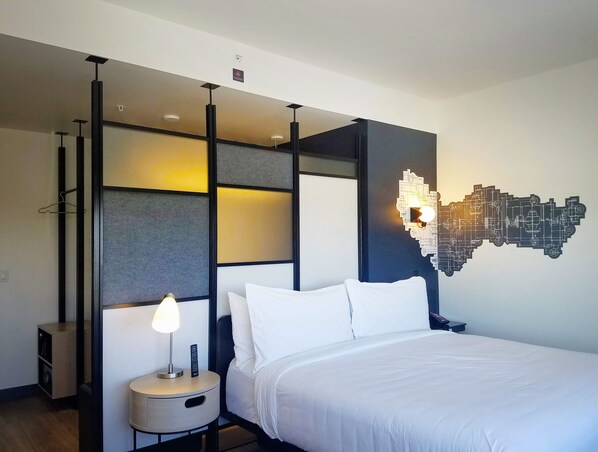 Una habitación de hotel moderna con una cama, una mesita de noche con lámpara, una lámpara de pared y una lámpara colgante.