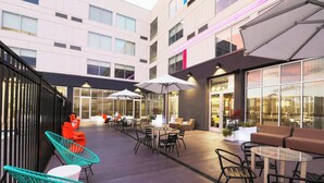 Un espace extérieur moderne aménagé avec des tables, des chaises et des parasols, entouré d’un bâtiment doté de grandes fenêtres et d’un escalier.