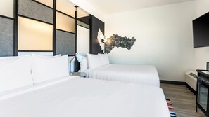 Habitación de hotel con dos camas, una obra de arte moderna en la pared, un escritorio con lámpara y un televisor de pantalla plana.