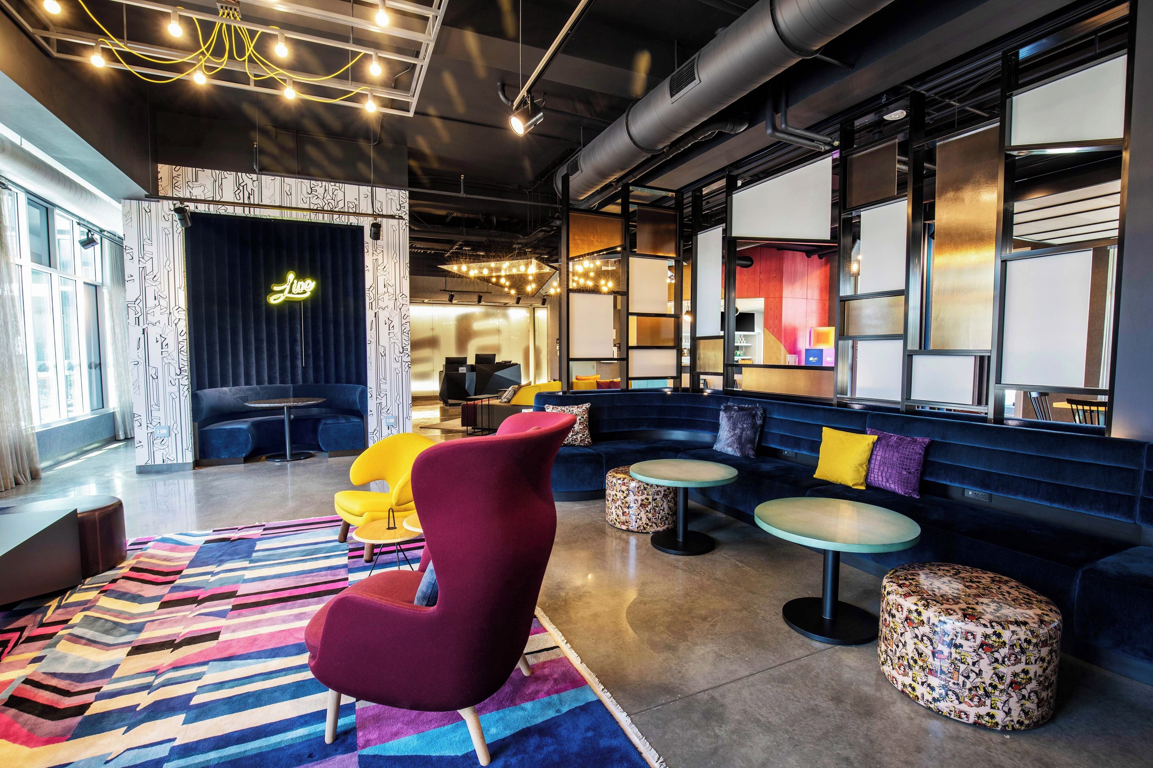 A modern lounge area with a dark blue sofa, a red chair, and a colorful striped rug.