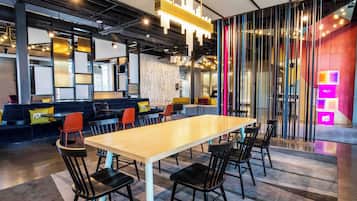 A modern hotel lobby with a long table and chairs, a reception desk, and a colorful wall with vertical stripes.