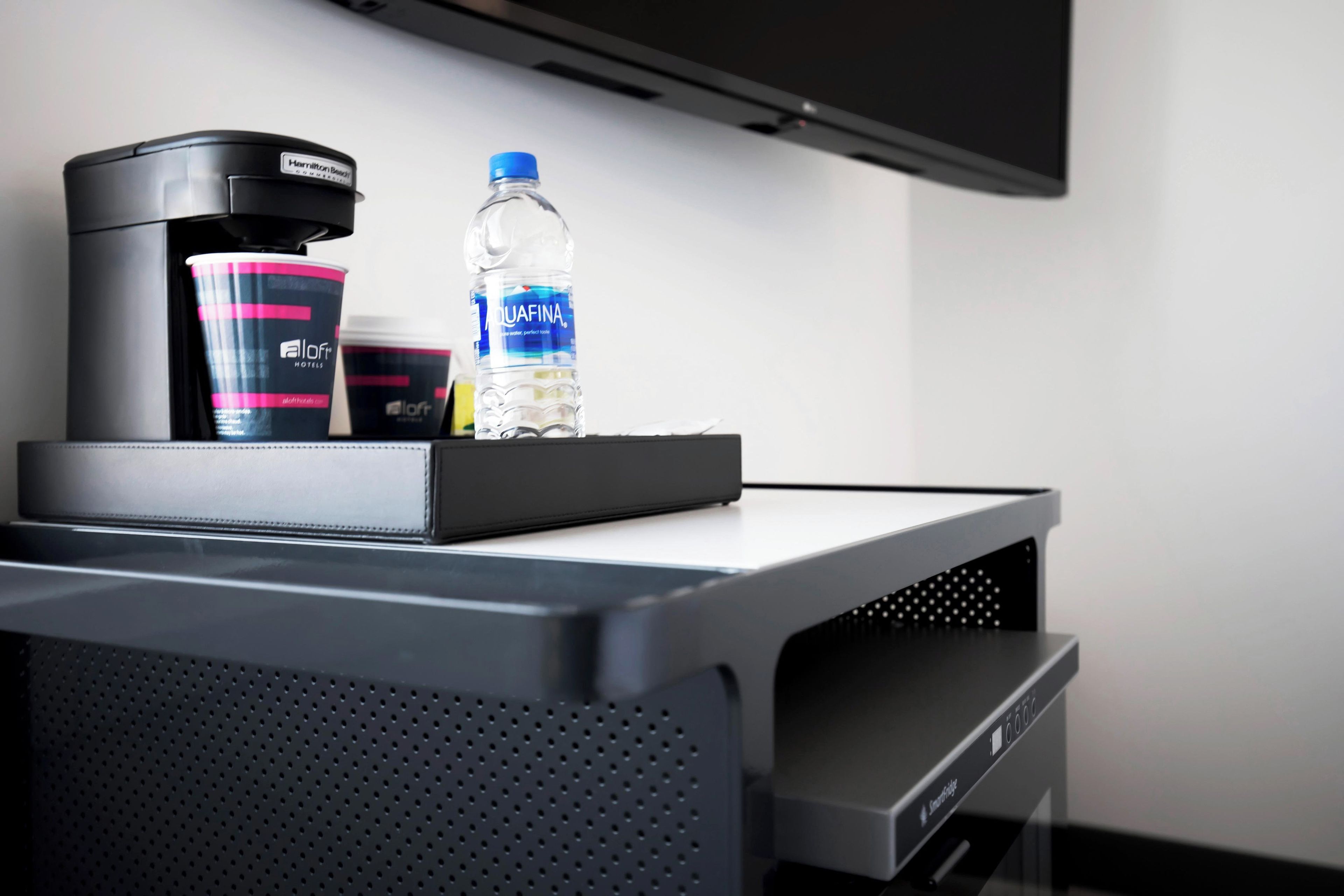 A minibar with a coffee maker, a water bottle, and a container of toiletries.