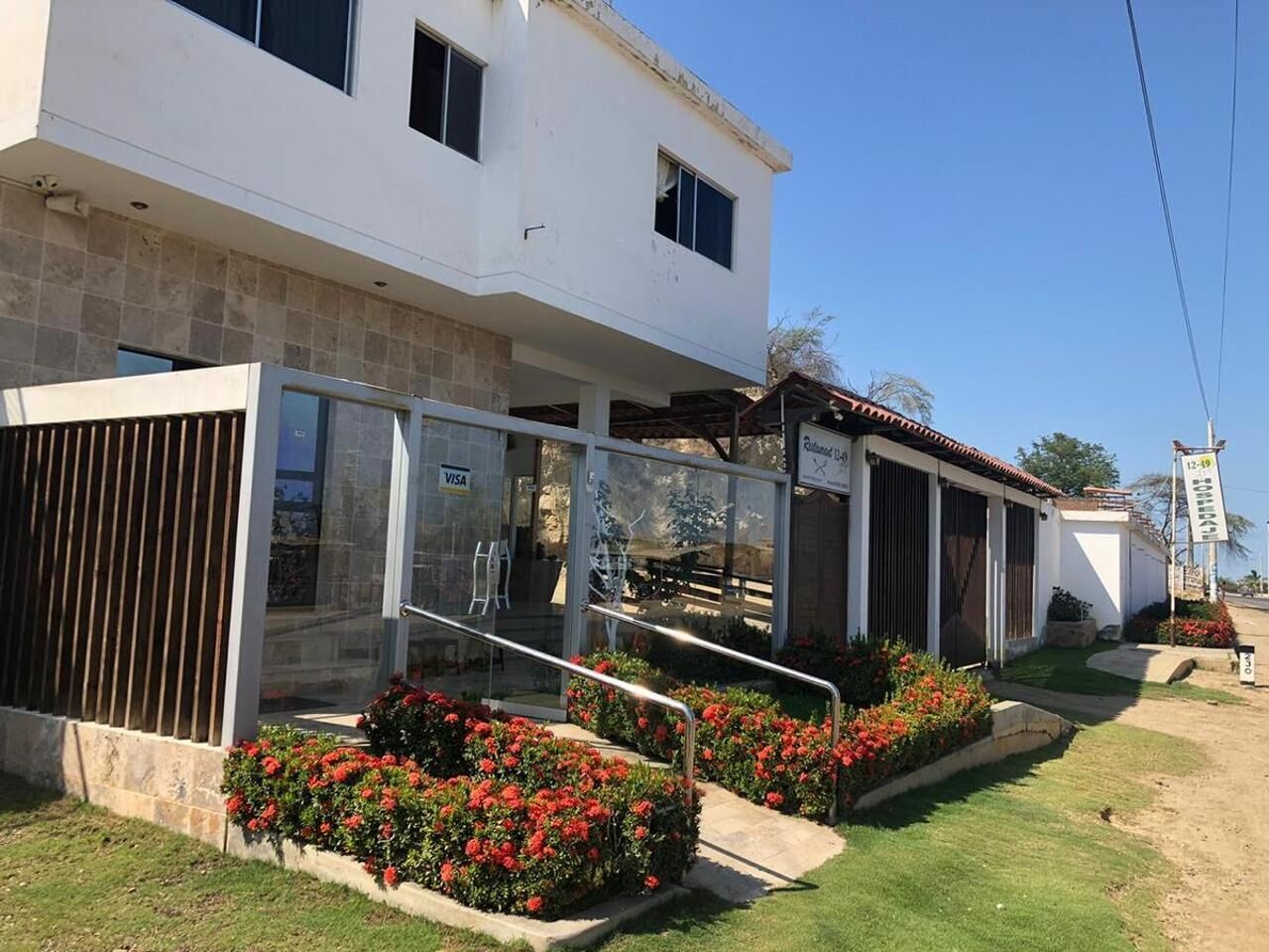 A modern two-story building with a glass entrance, a Visa sign, and a small outdoor seating area with red flowers.